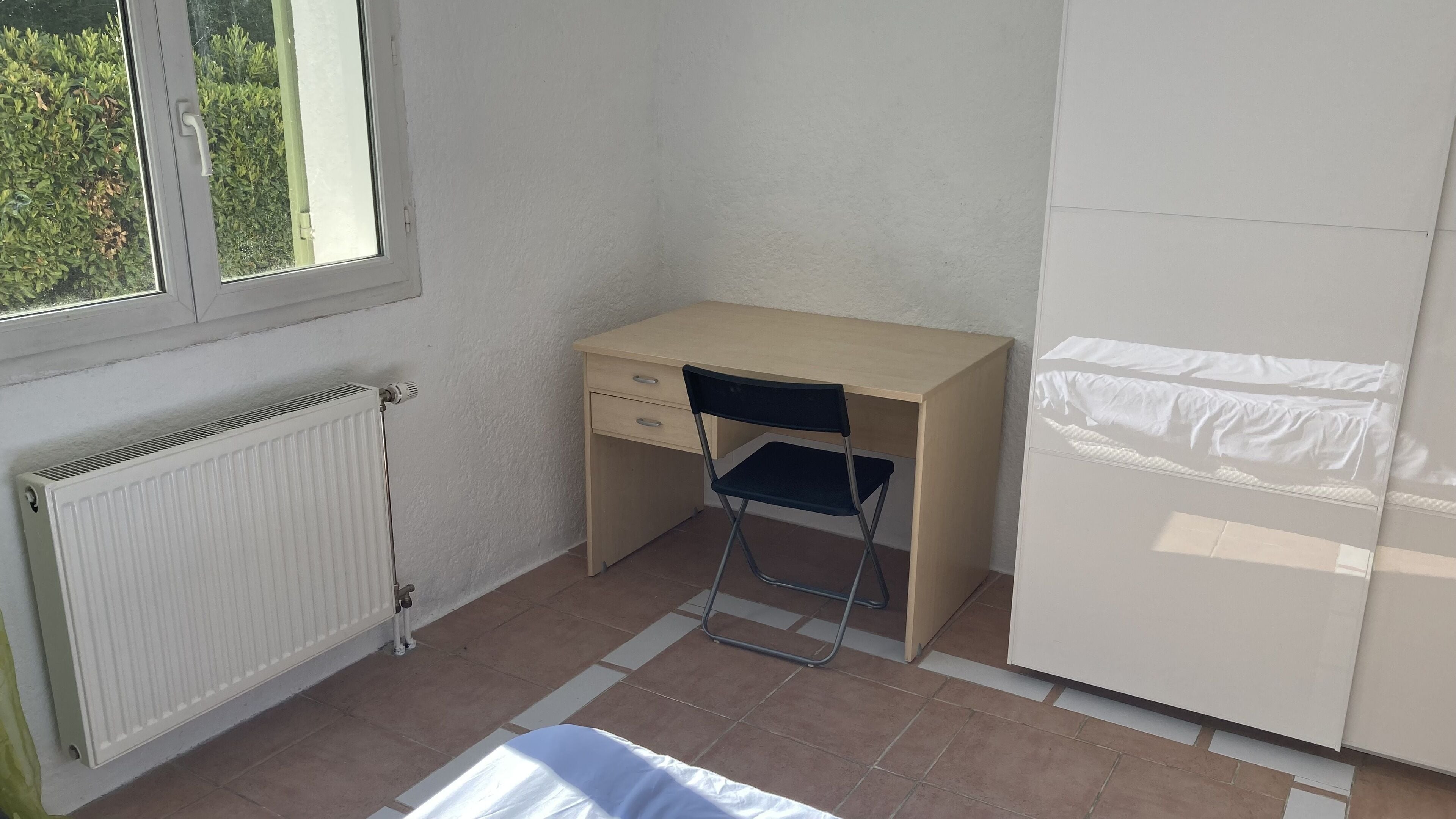 Une petite pièce bien éclairée, avec un bureau en bois, une chaise, un radiateur et une armoire.