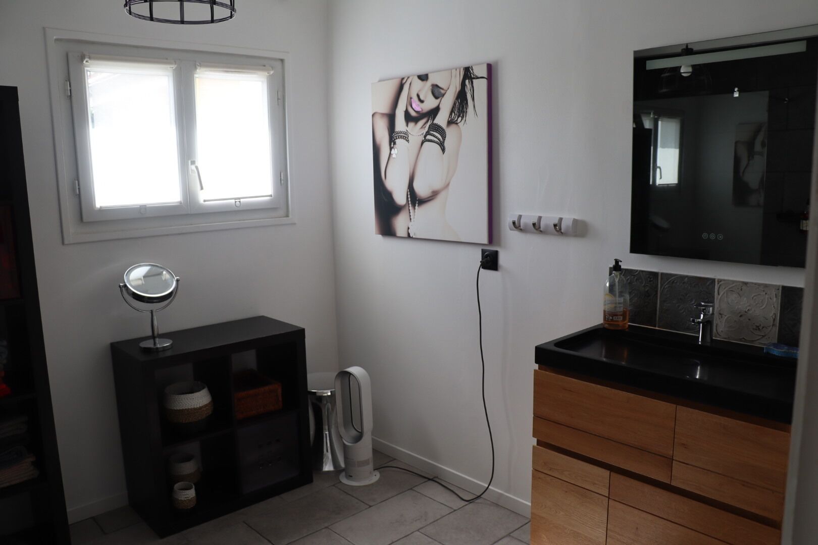 Un bagno con un mobile lavabo nero, uno specchio, un quadro appeso e una finestra.