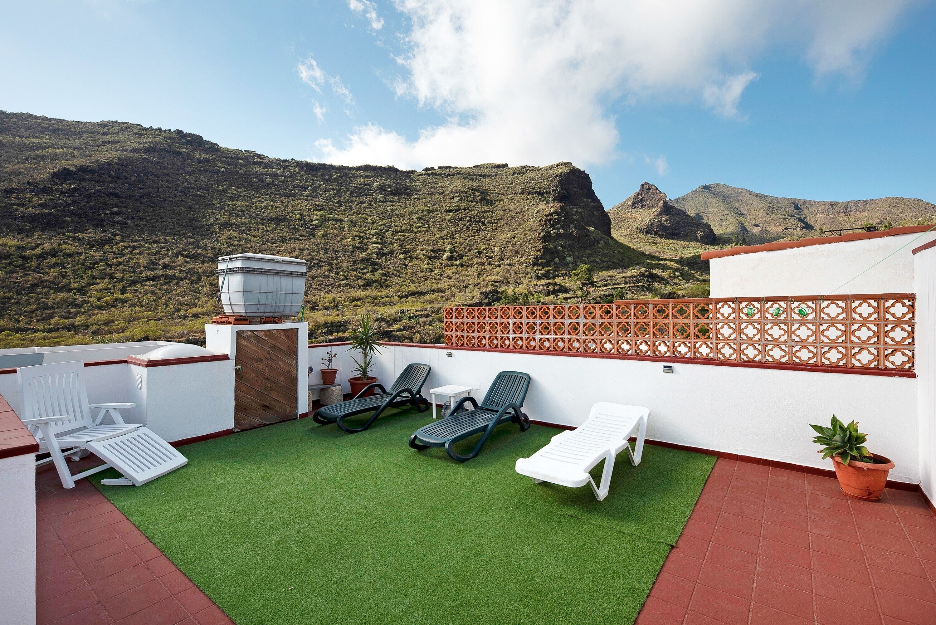 Terraço no telhado com grama sintética, cadeiras de descanso, um reservatório de água e vista para uma paisagem montanhosa.