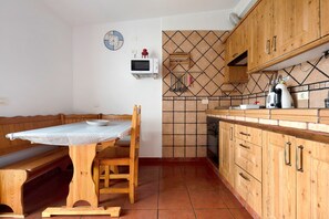 A kitchen with wooden cabinets, a tiled backsplash, a microwave, and a dining area with a bench and table.