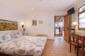 A bedroom with a bed, a desk, a chair, a TV, and a painting on the wall.