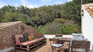 A terrace with a stone wall, wooden furniture, and a view of a hillside.