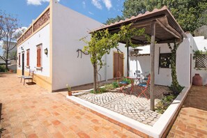 Um edifício branco com um pátio de azulejos, pérgola de madeira e área de estar ao ar livre.