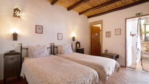 A room with two beds, a wooden nightstand, a wall-mounted lamp, and a door leading outside.