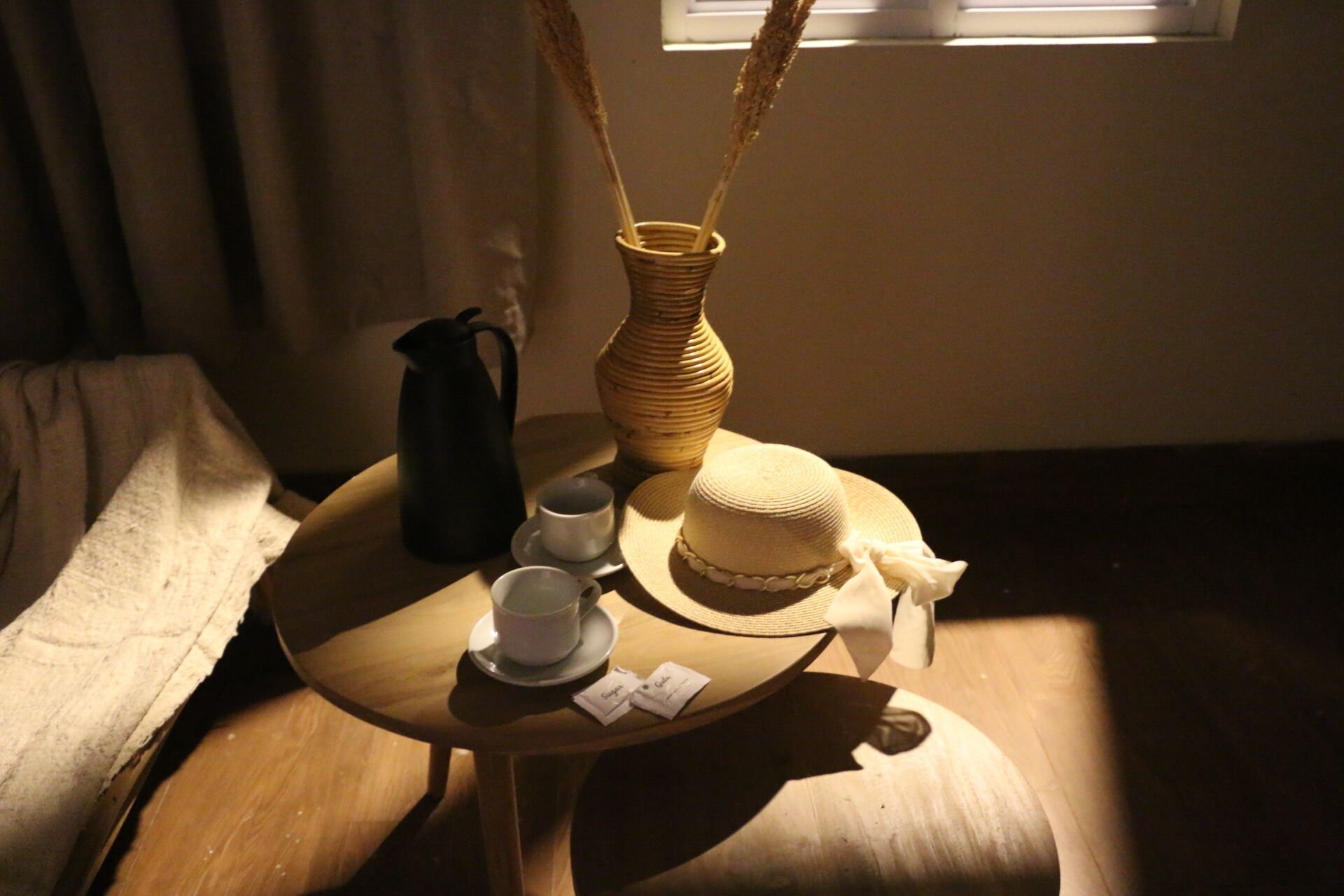 A small round table with a teapot, cups, and a hat.