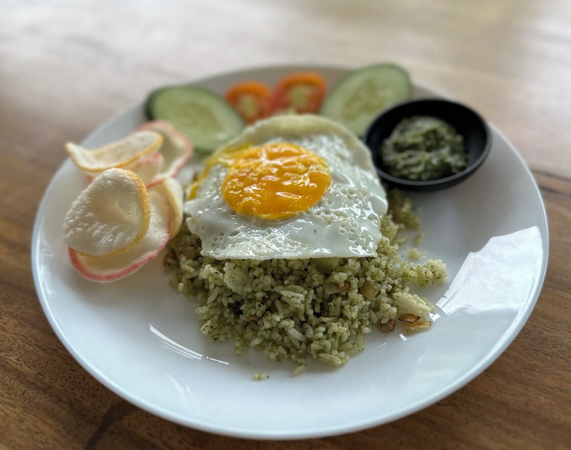 Une assiette contenant du riz frit, un œuf au plat, des tranches de concombre, des tranches de radis et un petit bol de sauce.