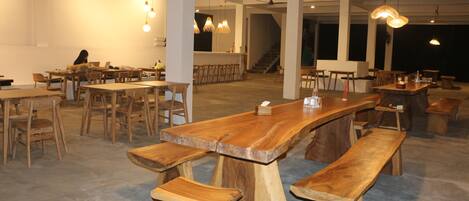 A spacious restaurant with wooden tables and benches, hanging pendant lights, and a visible staircase in the background.