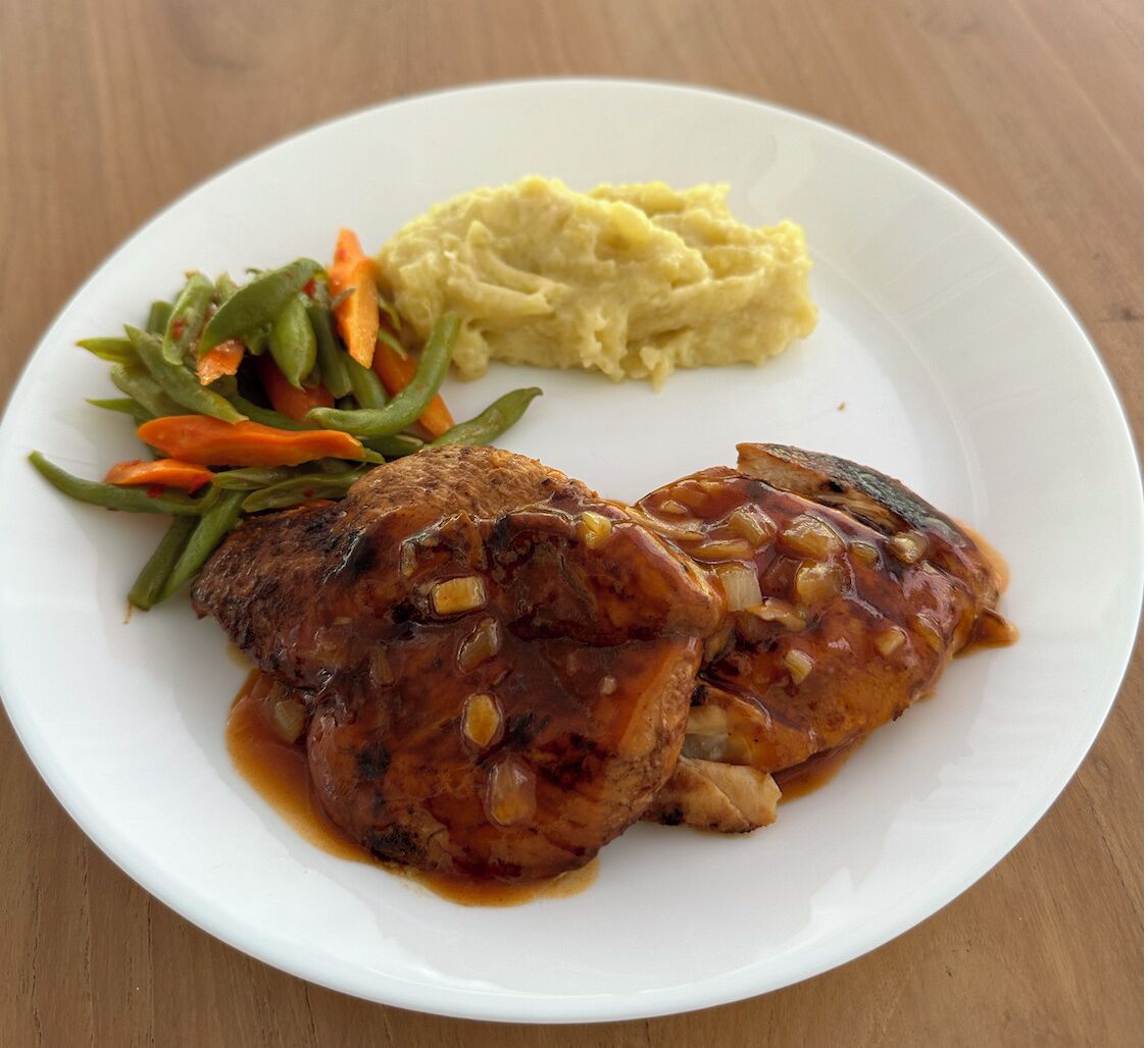 Une assiette comprenant un morceau de viande, de la purée de pommes de terre et un accompagnement de légumes variés.