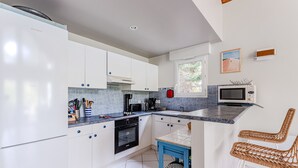 Une cuisine moderne avec des meubles blancs, un four encastré, une machine à café et un four à micro-ondes.