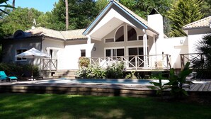 Une maison à deux étages dotée d’une grande véranda à l’avant, d’une piscine et d’un patio couvert.