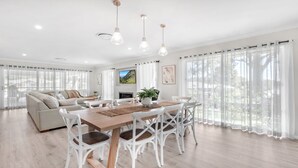 A spacious living room with a large sofa, a dining table with chairs, and a TV mounted on the wall. - D'VINE COTTAGE - THE VINTAGE HOLIDAY HOUSES (Rothbury)