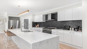 A modern kitchen with white cabinetry, a marble island, stainless steel appliances, and a black brick backsplash. - D'VINE COTTAGE - THE VINTAGE HOLIDAY HOUSES (Rothbury)