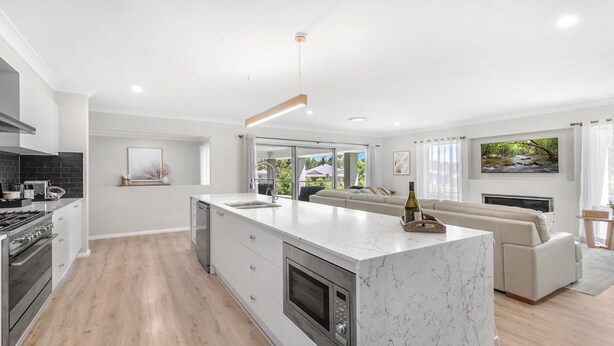 A modern kitchen with a large island, built-in oven, and a dining area with a sofa and a TV. - D'VINE COTTAGE - THE VINTAGE HOLIDAY HOUSES (Rothbury)