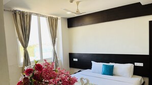 Une chambre d’hôtel avec un lit, un ventilateur de plafond, une fenêtre avec des rideaux et un vase rempli de fleurs.