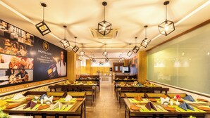 Un restaurant d’hôtel avec de nombreuses tables dressées pour les clients, une grande affiche promotionnelle accrochée au mur et un design moderne du plafond agrémenté de luminaires suspendus.