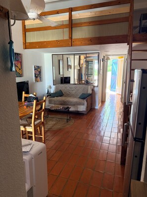 A cozy living area with a sofa, a dining table with chairs, a TV, and a ceiling fan.