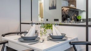 Ein moderner Essbereich mit einem weißen Tisch, gedeckt für zwei Personen, mit grauen Schüsseln, Besteck und weißen Servietten.