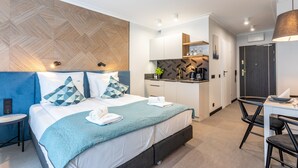 Ein modernes Hotelzimmer mit einem Bett, einem kleinen Schreibtisch, einem Stuhl, einer Küchenzeile und einem Badezimmer.