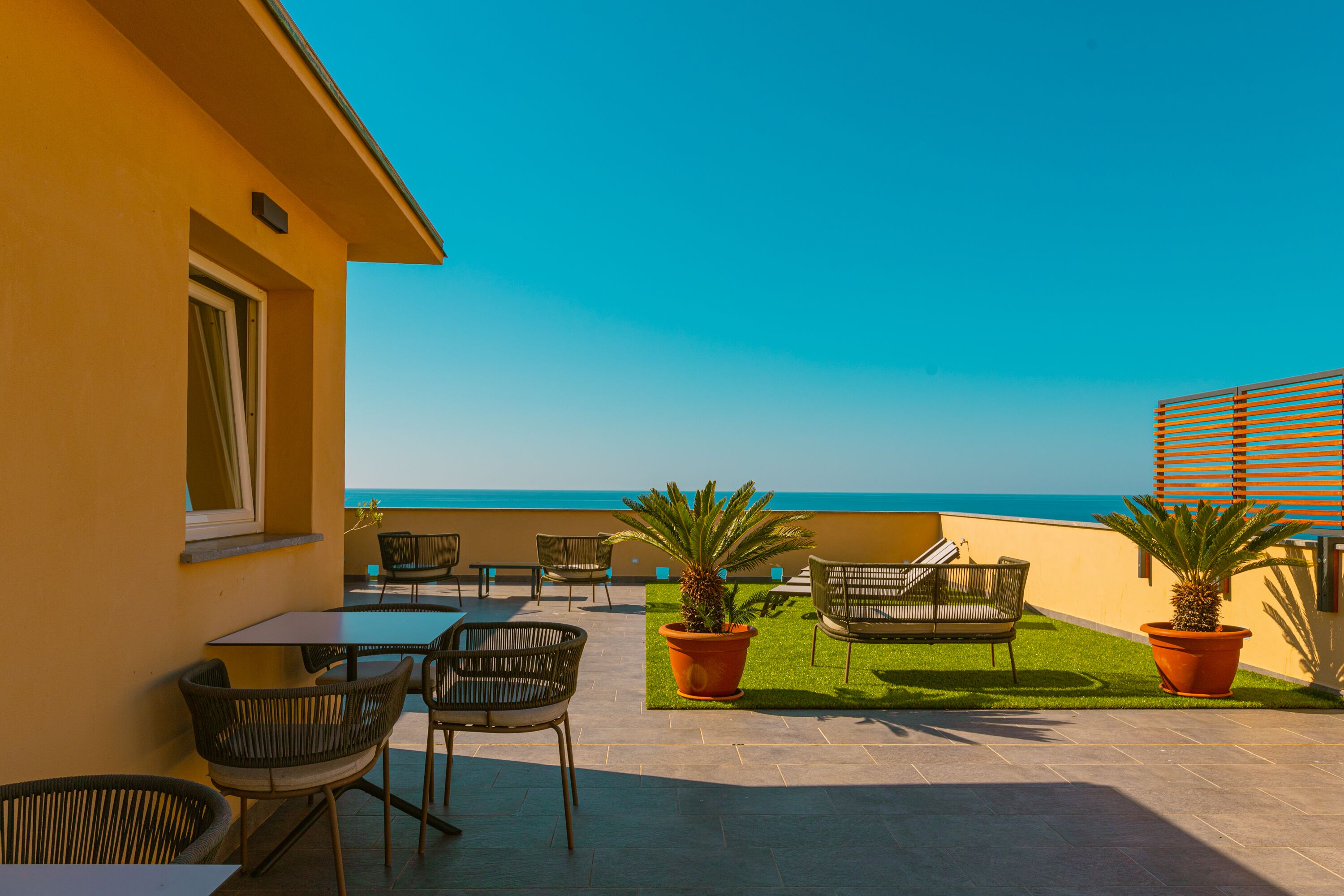 An outdoor patio with chairs and tables, a small lawn, and a view of the ocean.