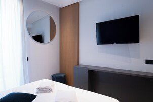 Una habitación de hotel moderna con una cama, un espejo redondo, un televisor en la pared y un taburete pequeño.