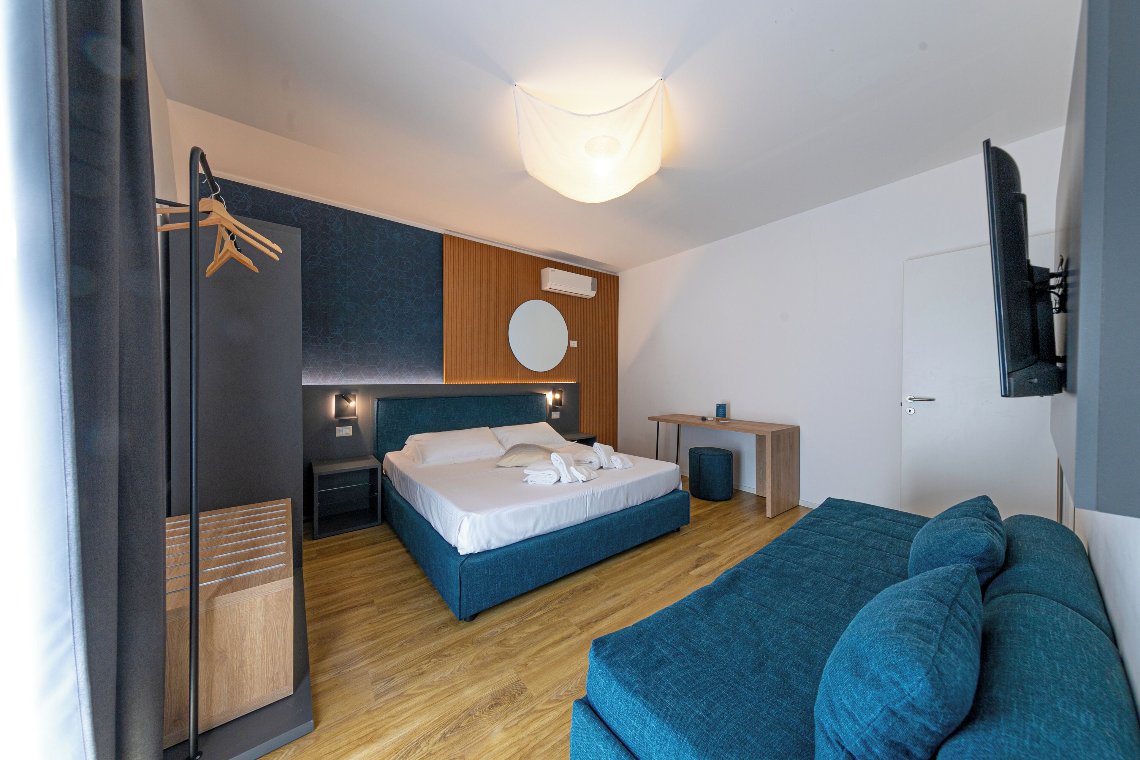 Quarto de hotel moderno com cama, sofá, escrivaninha e televisão.
