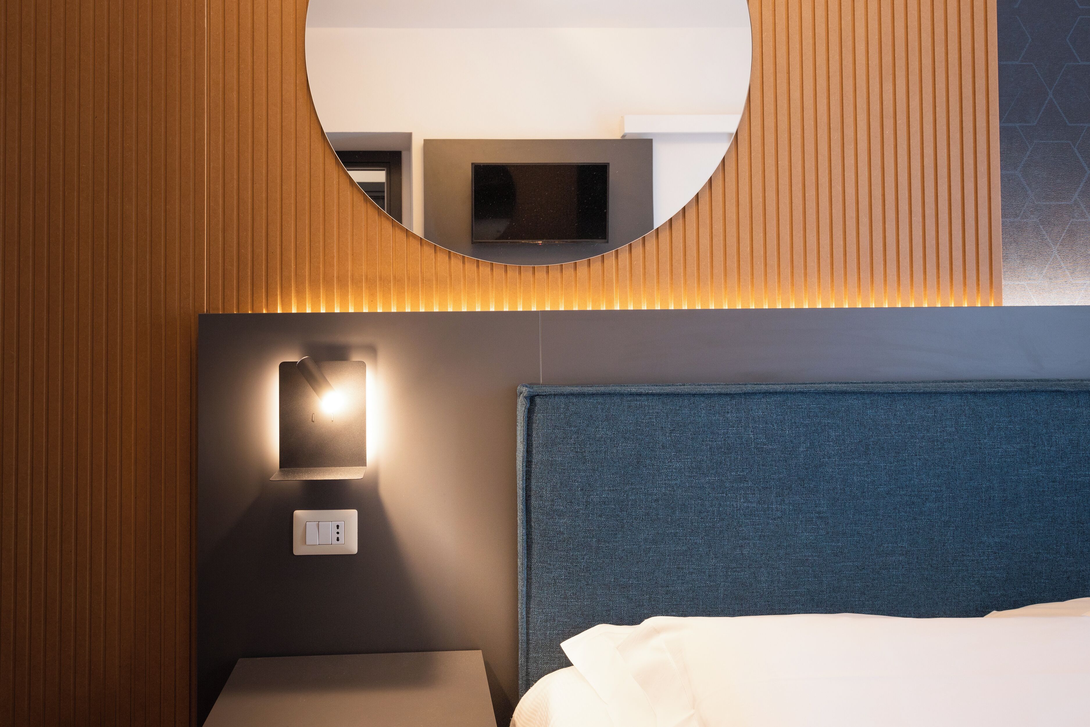 Une chambre d’hôtel avec un lit, une table de chevet, un téléviseur fixé au mur et un miroir.