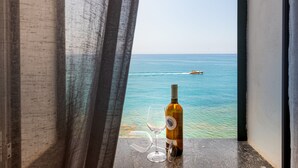A bottle of wine and a glass on a windowsill with a view of the sea and a boat in the distance. - Taliammari (Cefalù)