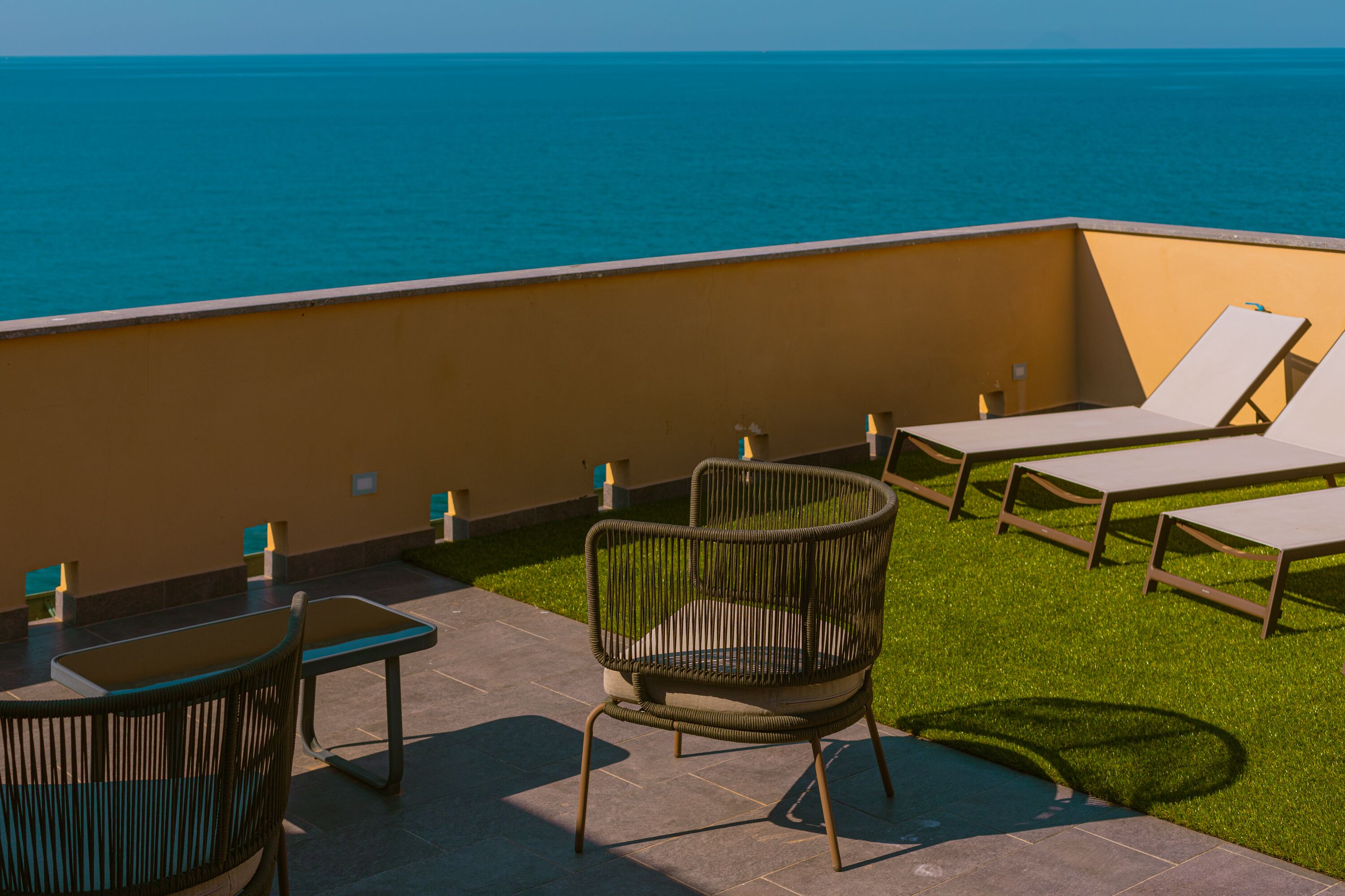 A terrace with a view of the sea, featuring lounge chairs, a table, and a chair.