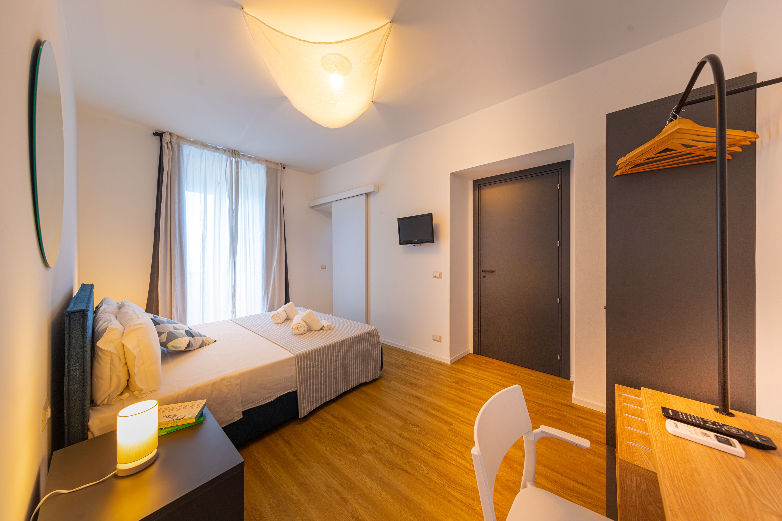 Ein Hotelzimmer mit Bett, Nachttisch, Lampe, Stuhl, Schreibtisch, Fernseher und einer Tür.