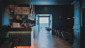 A modern bar area with a herringbone wood floor, bar stools, and a view of the sea through an open doorway. - Taliammari (Cefalù)
