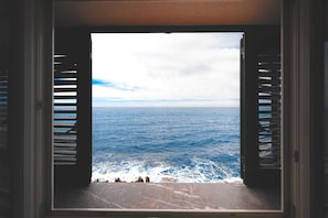 A view through a window with shutters, overlooking a body of water and rocky shoreline. - Taliammari (Cefalù)