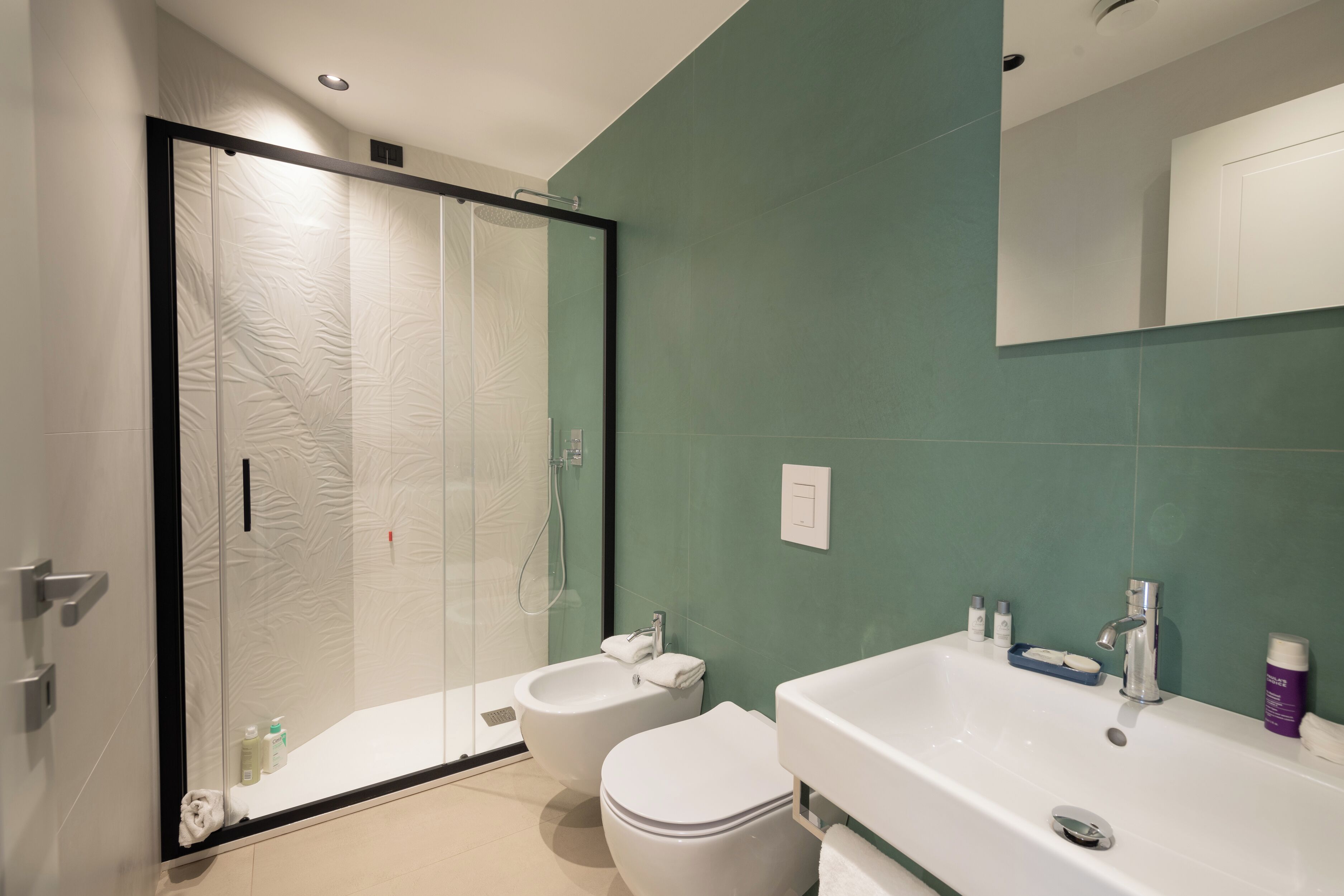 Un baño moderno con cabina de ducha de vidrio, un bidé, inodoro y un lavabo grande con espejo.