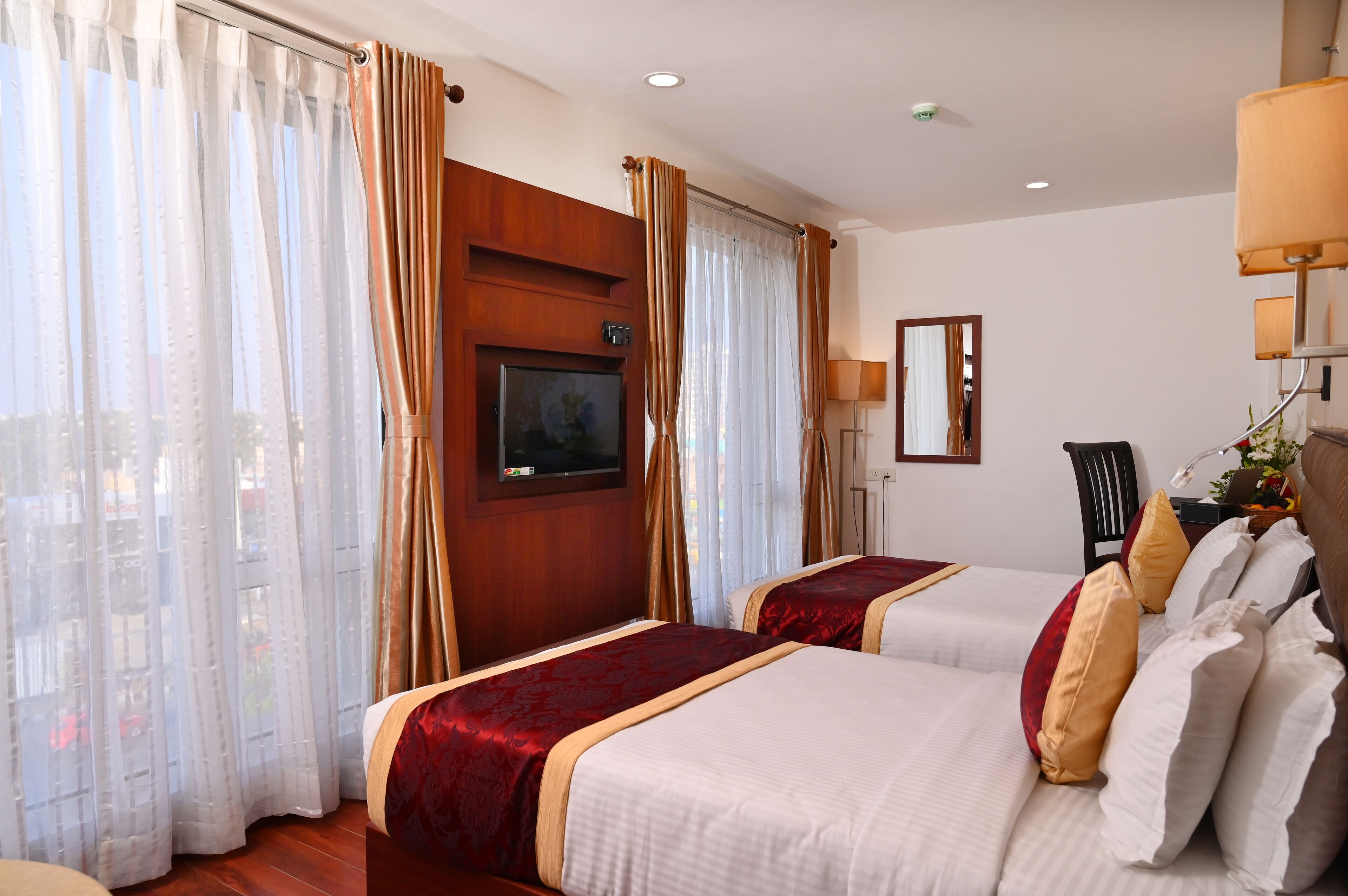 A hotel room with two beds, a TV, a desk with a lamp, and a window with curtains.