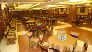 A banquet hall with multiple round tables, each with chairs covered in beige and purple fabric. - Raaj Bhaavan Clarks Inn Chennai (Chennai)
