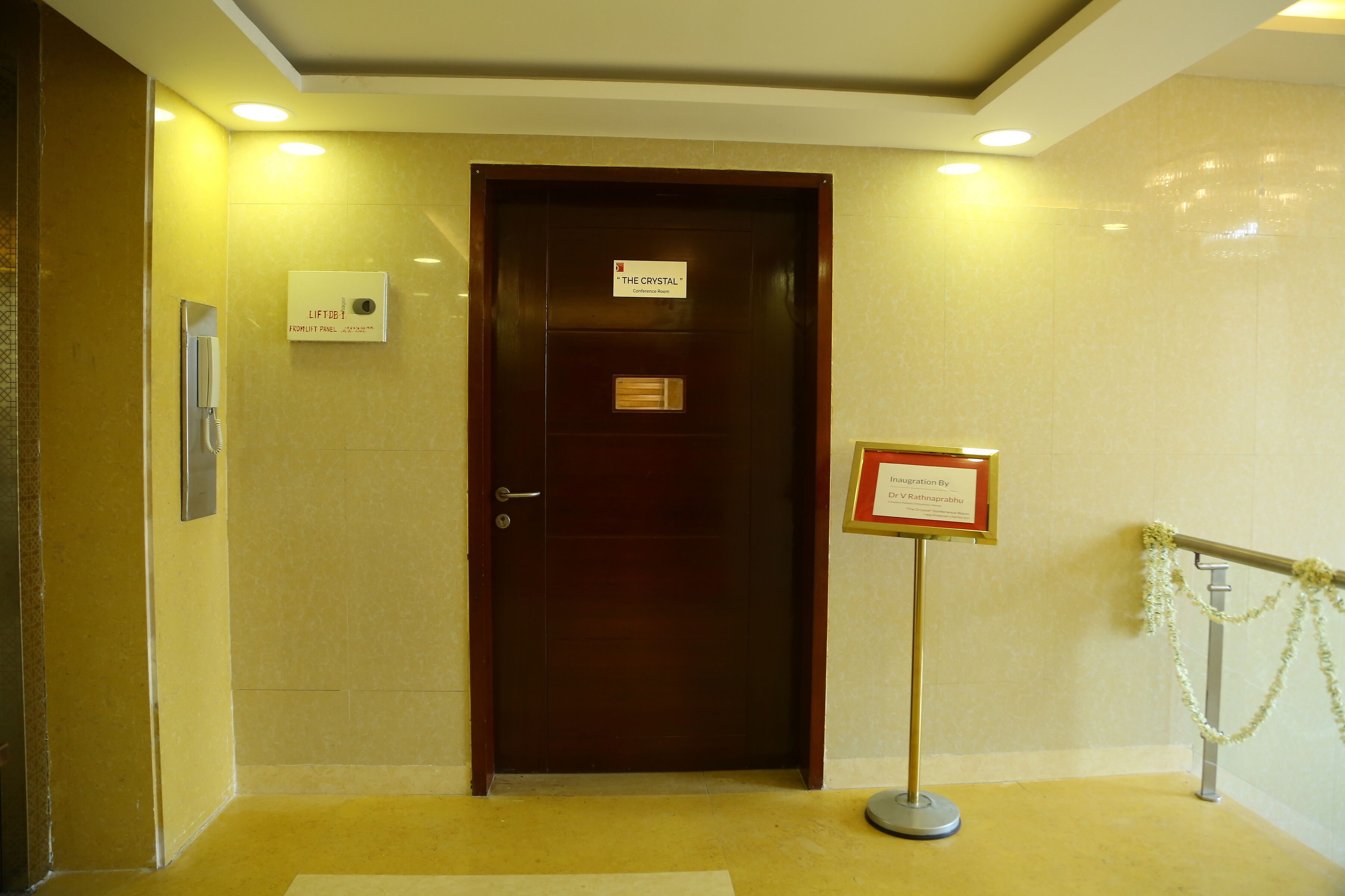 A hotel entrance with a wooden door, a lift call button, and a sign indicating 'The Crystal' hotel.