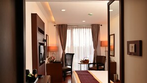 A hotel room with a bed, a desk with a lamp, a chair, a small table with a basket, and a mirror on the wall. - Raaj Bhaavan Clarks Inn Chennai (Chennai)