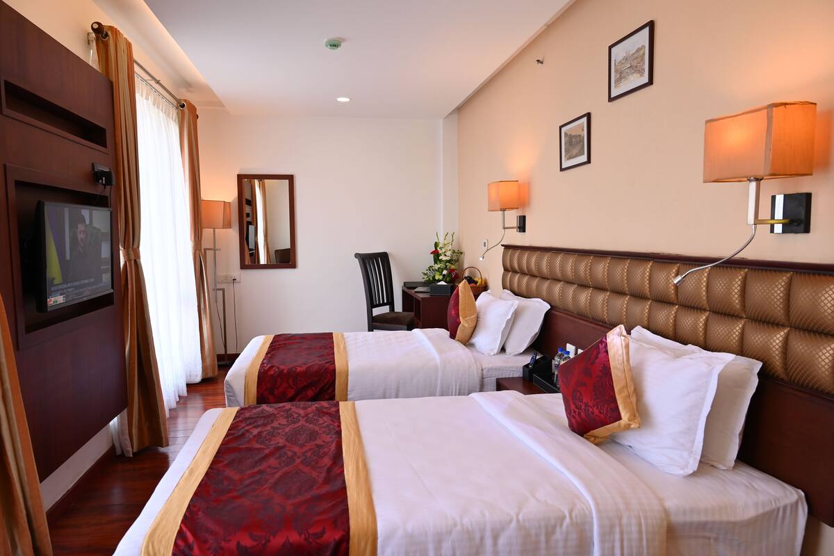 Habitación de hotel con dos camas, televisión, espejo y lámparas fijadas a la pared.