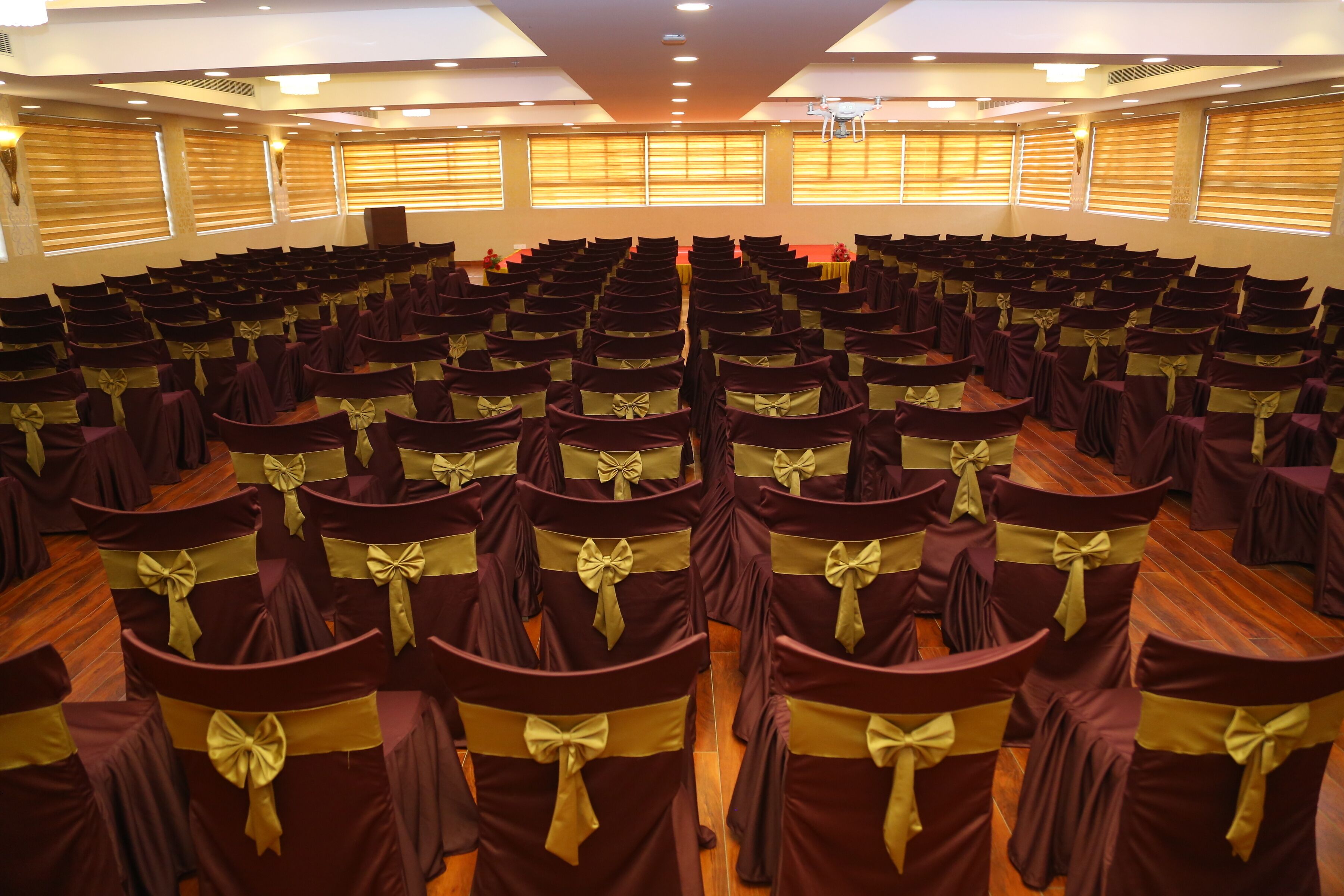 A conference room with rows of chairs, each with a gold sash and bow, arranged in a semi-circle facing a stage.