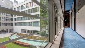 Un bâtiment moderne doté de grandes fenêtres, d’une cour agrémentée d’un élément décoratif aquatique et d’un plafond bleu.