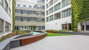 Un bâtiment moderne doté d’une cour intérieure comprenant un banc en bois aux lignes courbes, des jardinières et un petit élément décoratif aquatique.