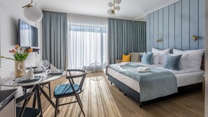 Une chambre d’hôtel moderne équipée d’un lit, d’un bureau avec une chaise, d’une télévision et d’une grande fenêtre avec des rideaux.