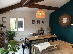Un espace repas avec une table et un banc en bois, entouré de plantes en pot, sous un luminaire suspendu.