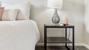 A bedroom with a bed, a nightstand with a lamp, and a framed picture on the wall. - Beautiful home w/easy access to anywhere in Tulsa! (Tulsa)