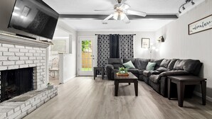 A living room with a fireplace, a flat-screen TV, a leather sofa, and a ceiling fan. - Beautiful home w/easy access to anywhere in Tulsa! (Tulsa)