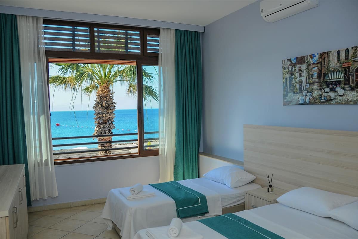 A hotel room with two beds, a view of the sea, and a painting on the wall.