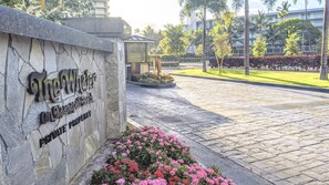 A stone wall with a sign for 'The Whaler On Kaua'i Property' and a paved area with flowers.