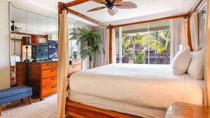 Une chambre à coucher avec un lit à baldaquin, une commode en bois, une télévision et une grande fenêtre donnant sur des palmiers.