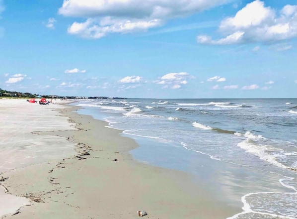 Ein Strand mit Wellen, blauem Himmel und Gebäuden in der Ferne.