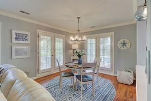 A dining area with a chandelier, round table, chairs, and a vase with flowers.