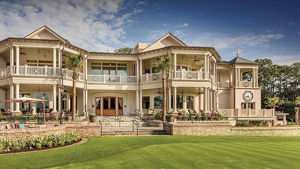 A large, two-story house with multiple balconies, a well-maintained lawn, and outdoor seating areas.